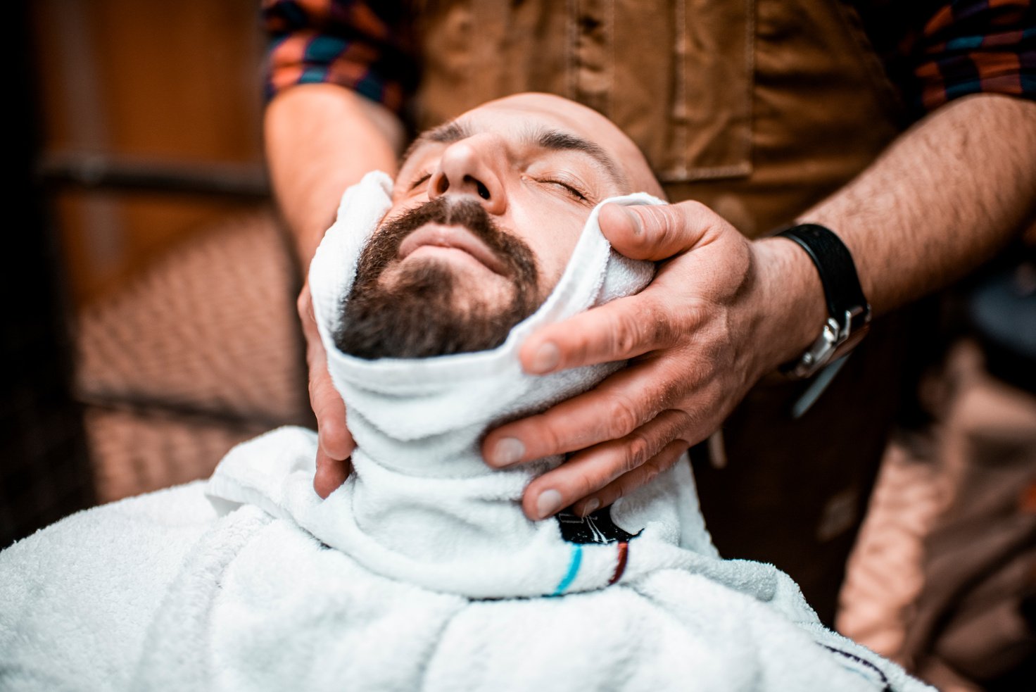 Barber putting a hot towel on a male's face before giving him a shave in a barber salon